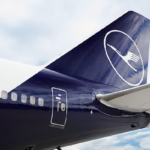En la cola y el alerón trasero de un avión de pasajeros, ambos de color azul, se puede ver el logo de la aerolínea Lufthansa, en color blanco.